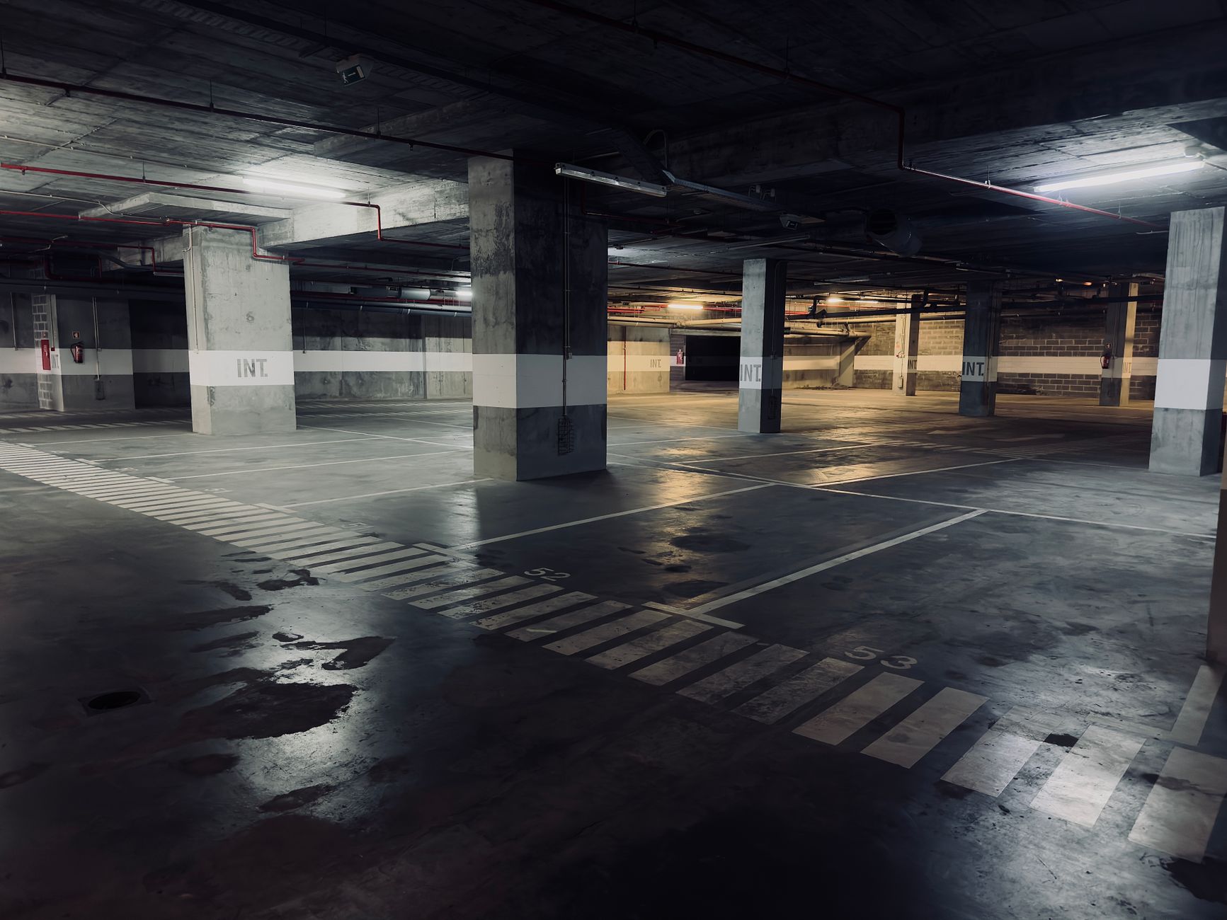 Dimly lit underground parking garage with empty spaces and puddles on the floor.