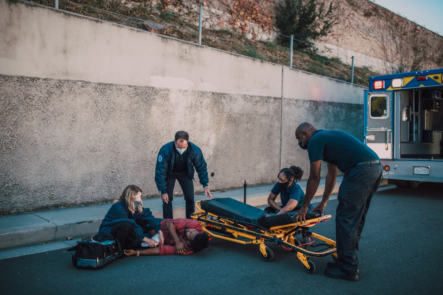 Emergency medical team assists an injured person on the street with a stretcher nearby.