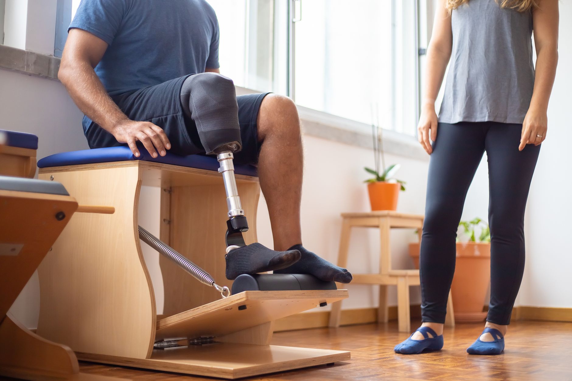 Man with prosthetic leg doing rehabilitation exercises alongside a trainer in a gym.