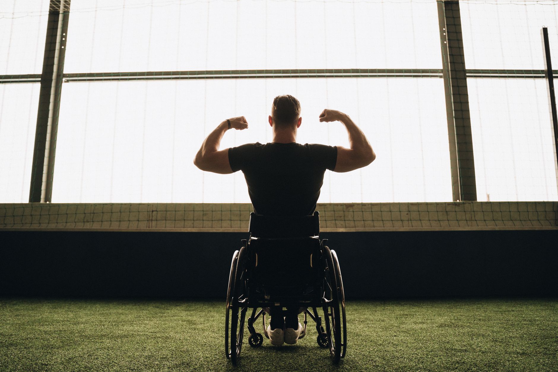 Rear view of a muscular man in a wheelchair flexing his arms in a sports facility.