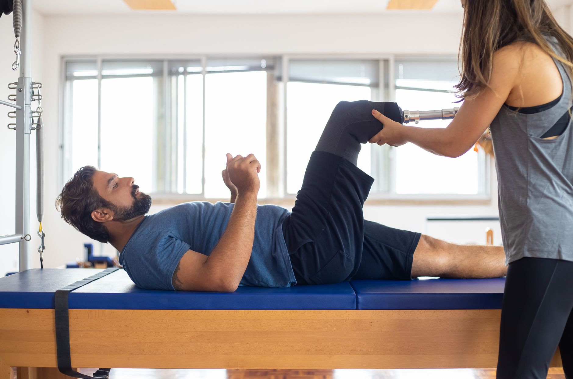 Therapist assists man with prosthetic leg during a physical rehabilitation session.