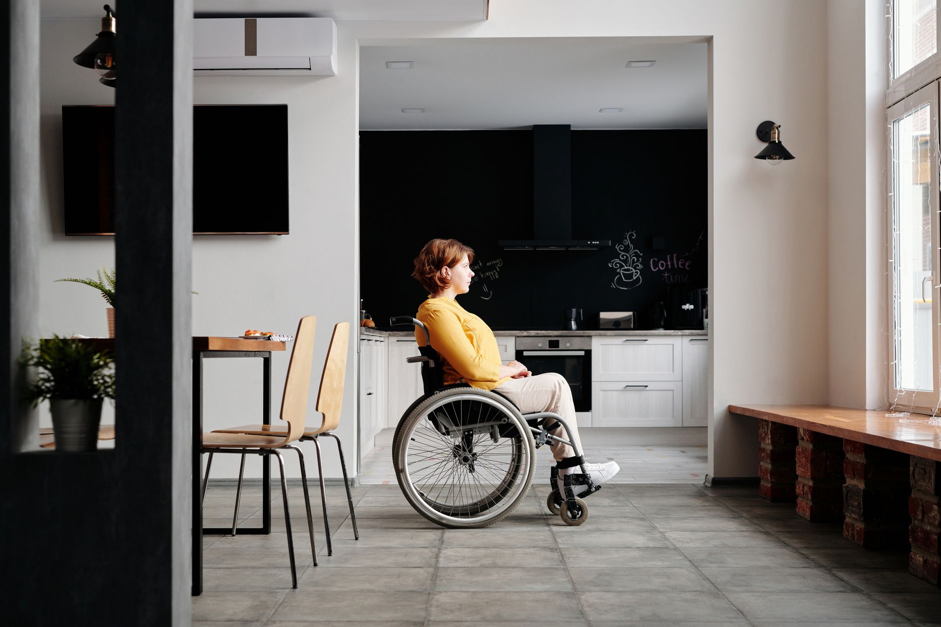 Woman using a wheelchair looking out a window in a stylishly decorated modern home.