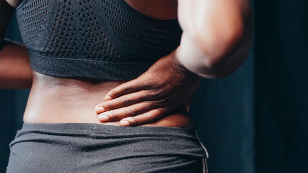 Adult holding their lower back in pain, indicating possible lower spine discomfort or injury.