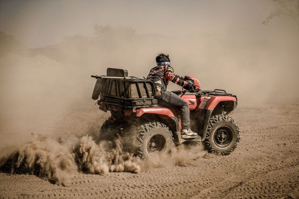 Adult riding quad bike on dusty off-road trail.