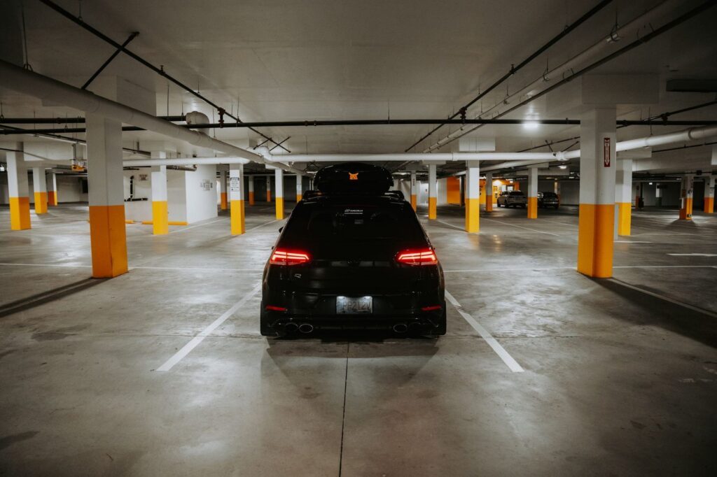 Black car parked in underground garage with concrete pillars.