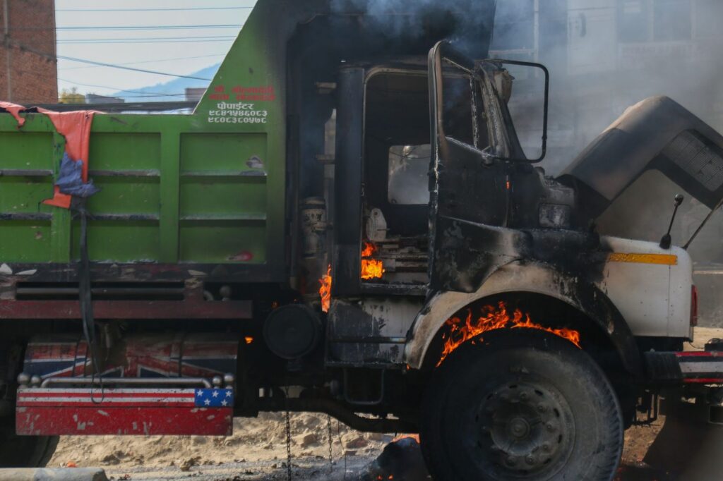 Burning truck engulfed in flames and smoke on city street.