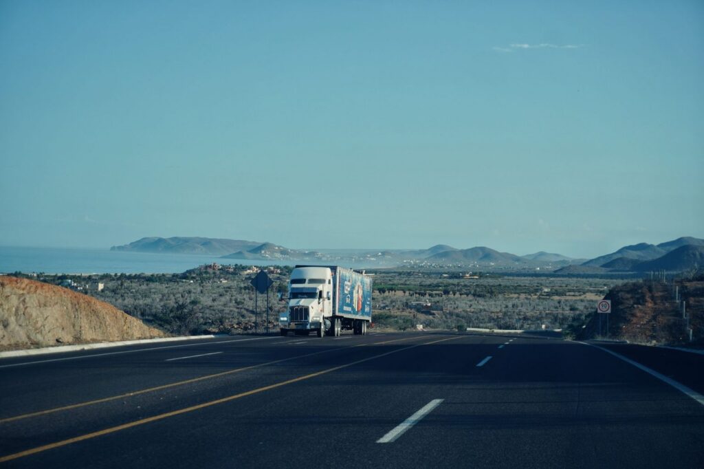 Camión semi remolque circulando por carretera con montañas de fondo bajo cielo despejado.
