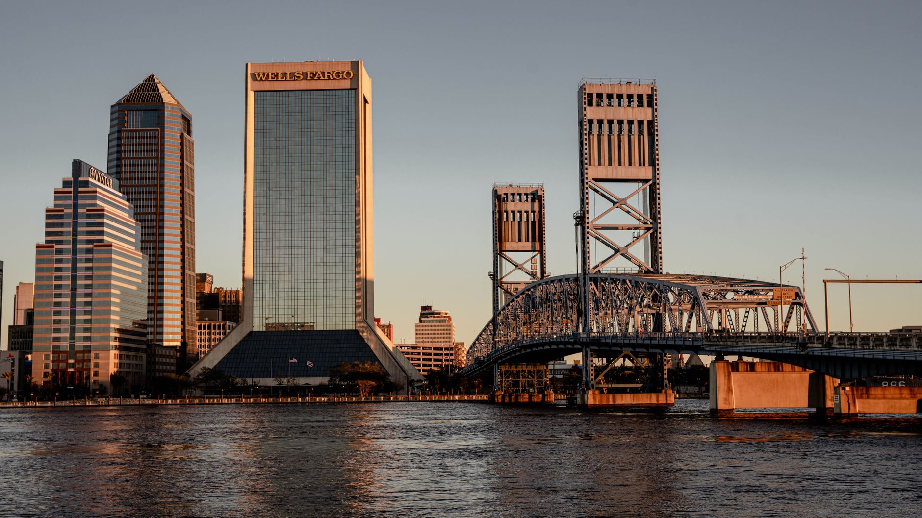 Jacksonville, FL skyline at sunset with bridges and skyscrapers reflecting on the river.