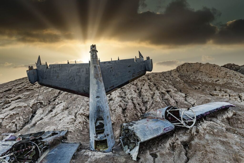 Crashed aircraft wreckage in desert landscape at sunset.