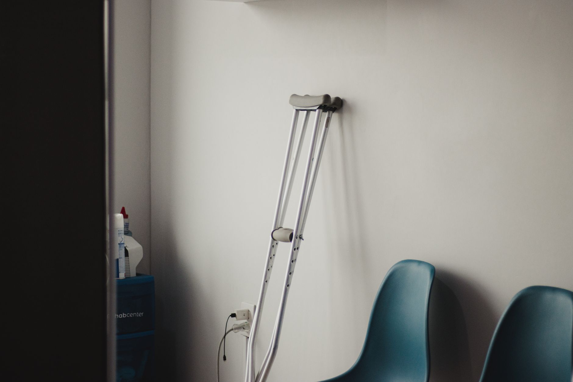 Crutches leaning against a wall beside blue chairs in a minimalist medical waiting room.