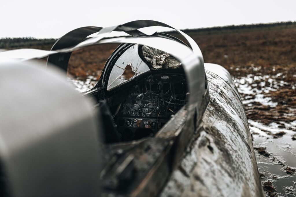Damaged aircraft cockpit wreckage in an empty field after a crash.