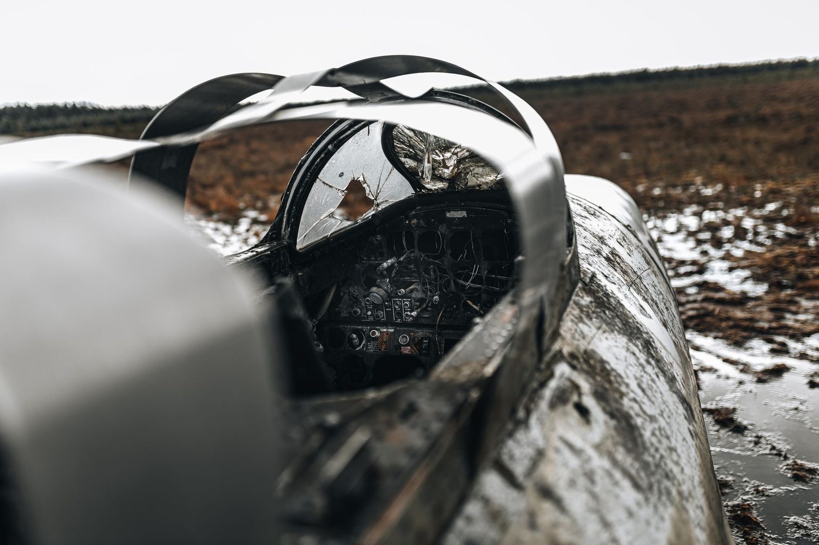 Damaged military aircraft cockpit wreckage in an empty field.