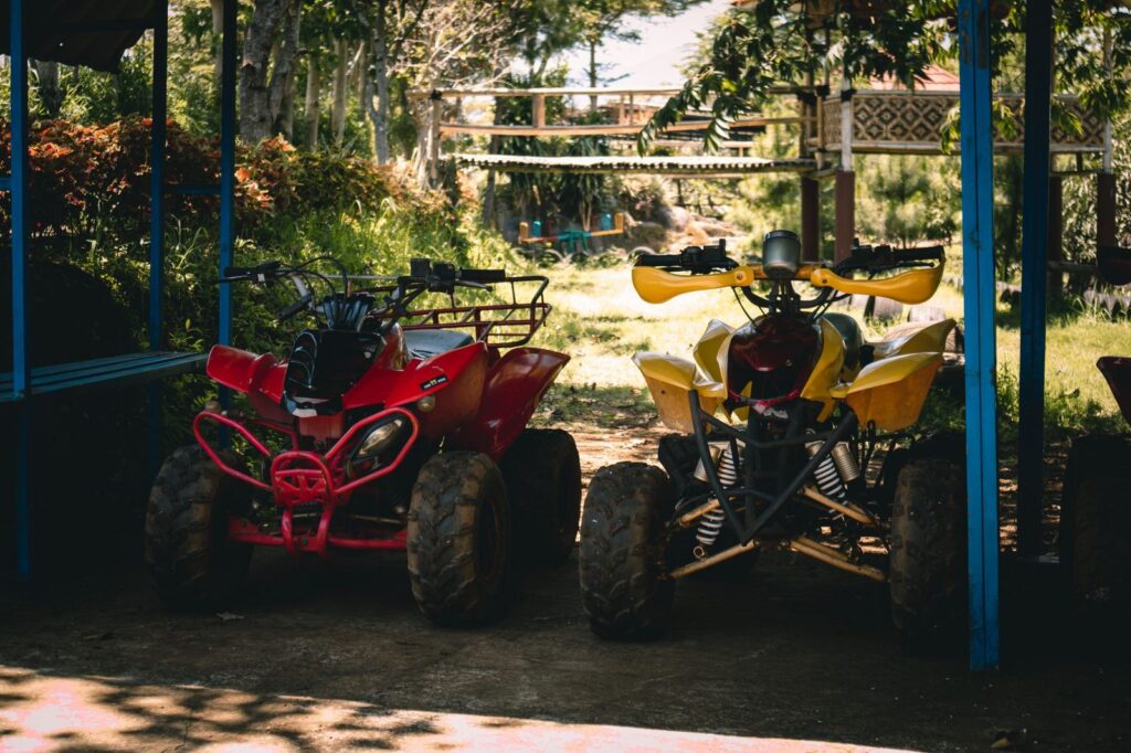 Dos motos cuatrimotos estacionadas bajo sombra rodeadas de vegetación exuberante.