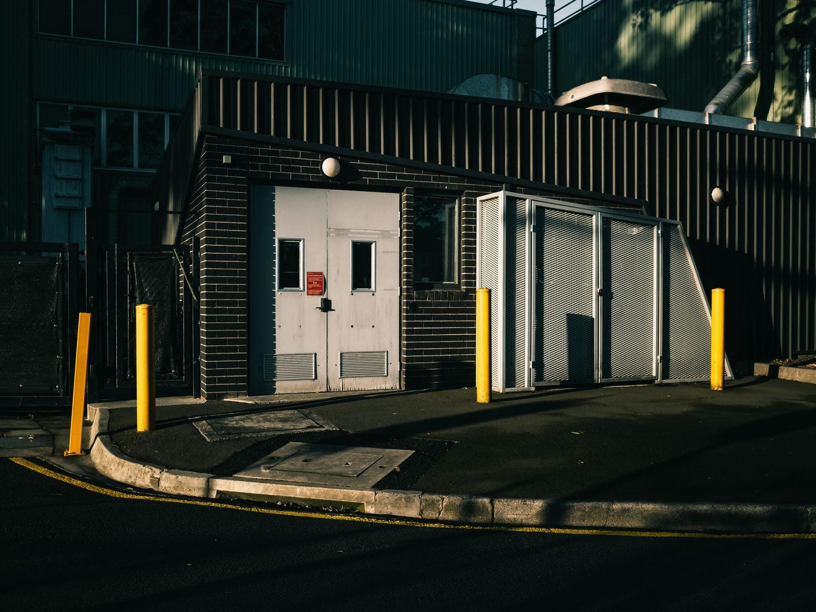 Edificio industrial con puertas metálicas y bolardos de seguridad en la entrada.
