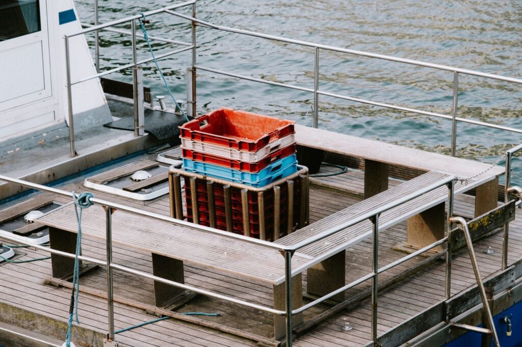 Empty fishing boat deck with stacked colorful crates and calm water.