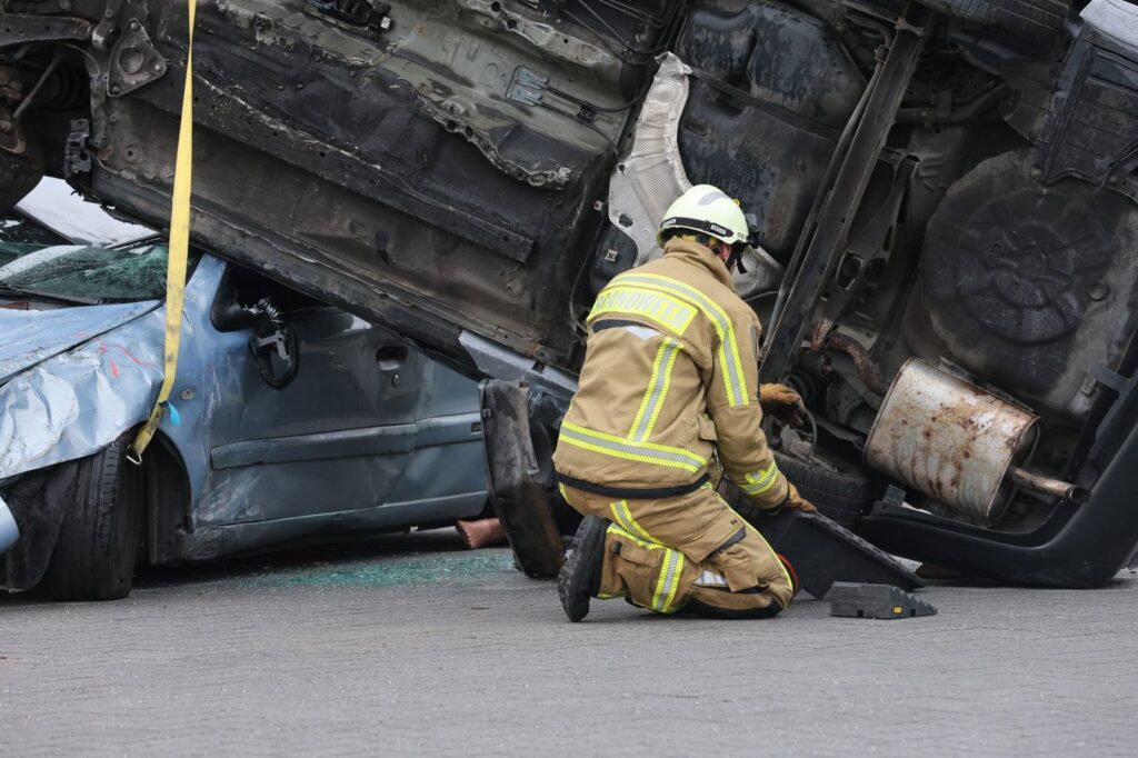 Firefighter in protective gear assisting at overturned vehicle crash scene.