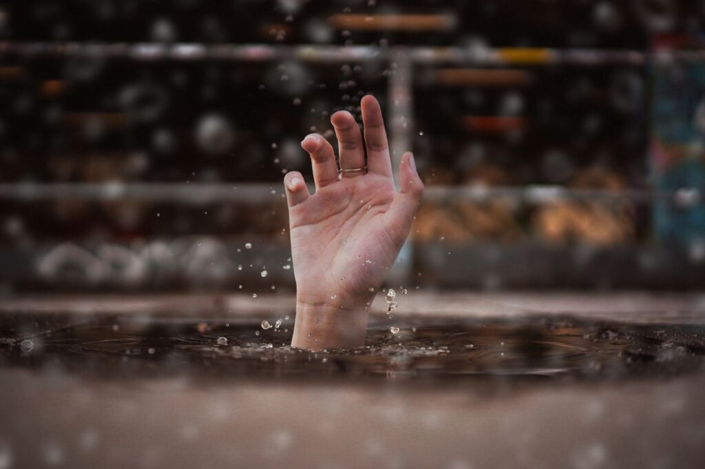 Hand reaching from water surface in rain, symbolizing drowning emergency.