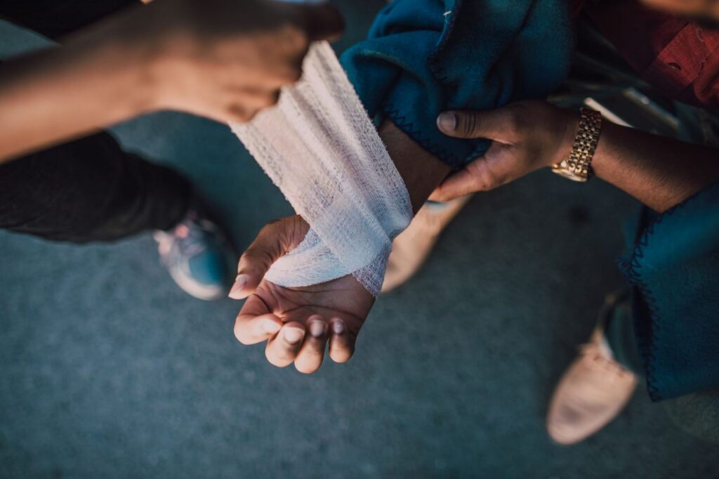 Hands applying a bandage to an injured wrist outdoors.