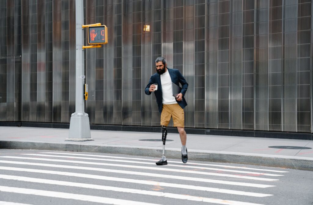 Hombre con pierna protésica sostiene café y tablet en entorno urbano.
