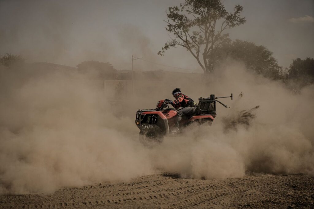 Hombre conduciendo un quad por terreno polvoriento fuera de carretera.