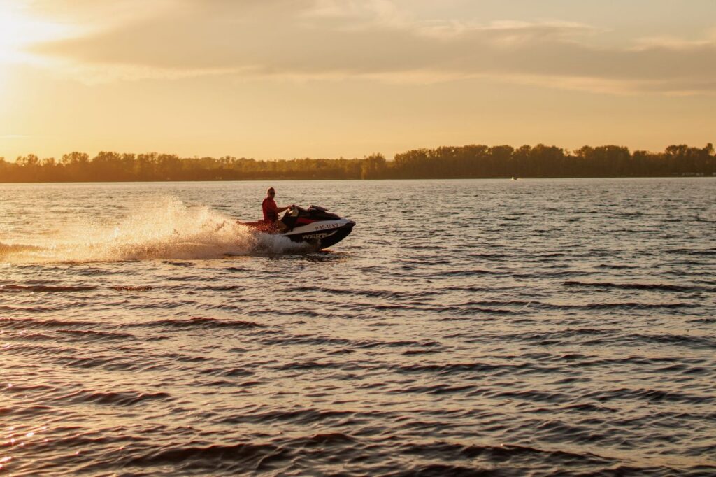 Jet ski speeding across a lake at sunset with water spray.