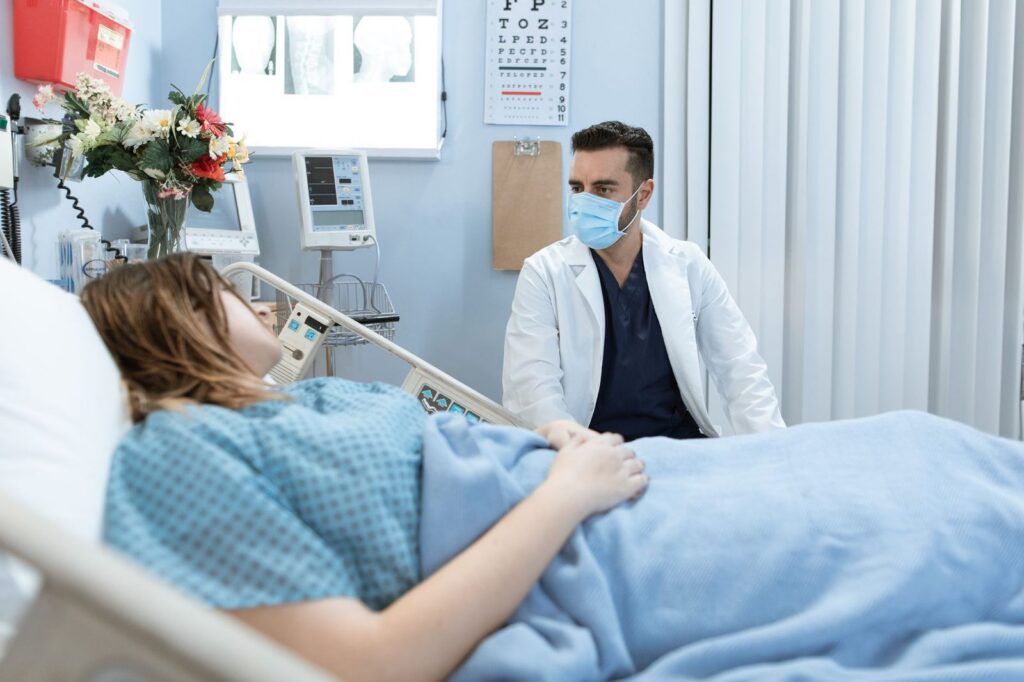 Médico con mascarilla consulta a paciente en cama de hospital.