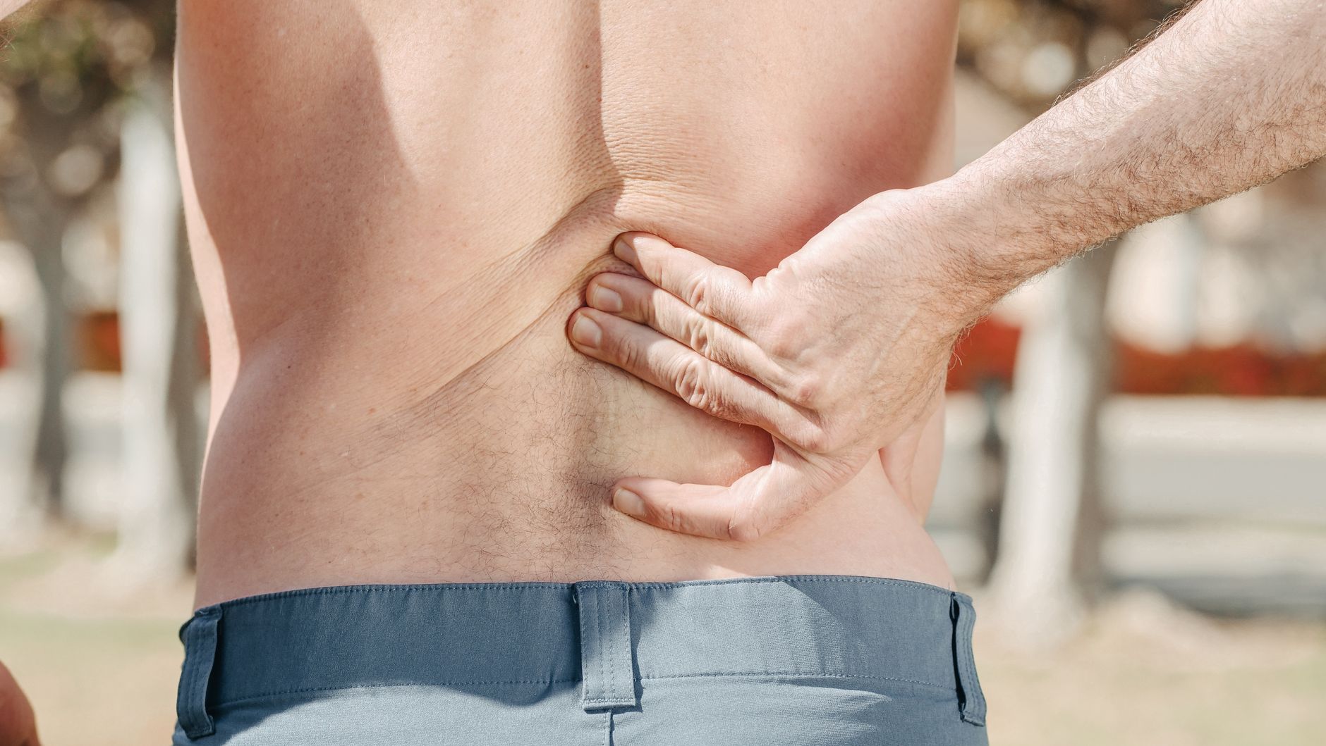Man clutching his lower back in pain, indicating a possible spinal injury.