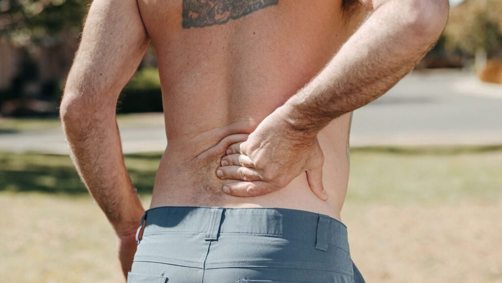 Man holding lower back outdoors with pain expression.