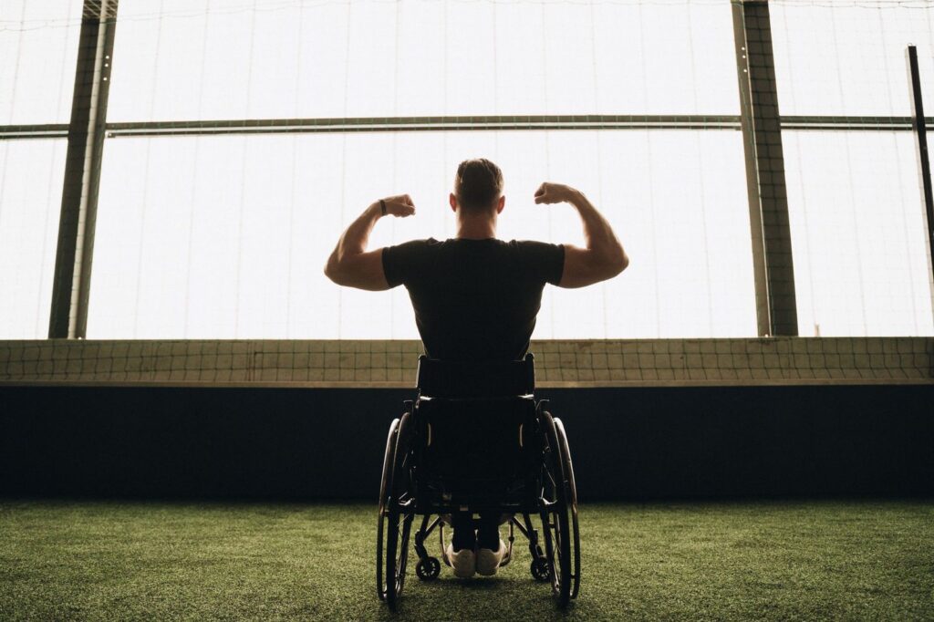 Man in wheelchair flexing muscles in sports facility.