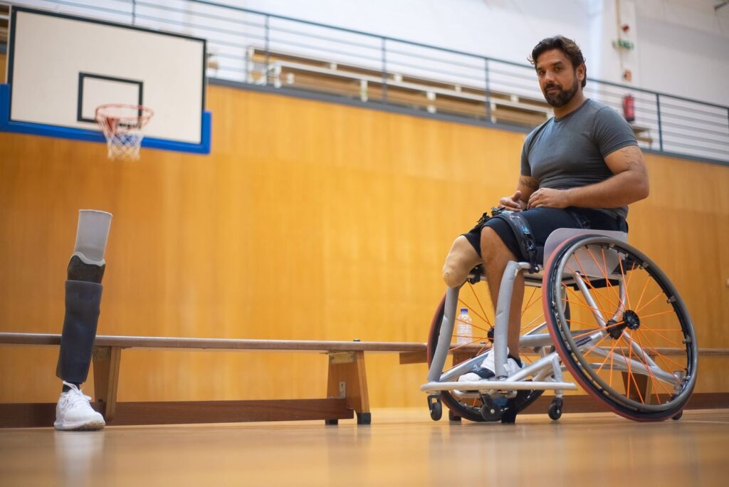 Man in wheelchair with prosthetic leg on indoor basketball court.
