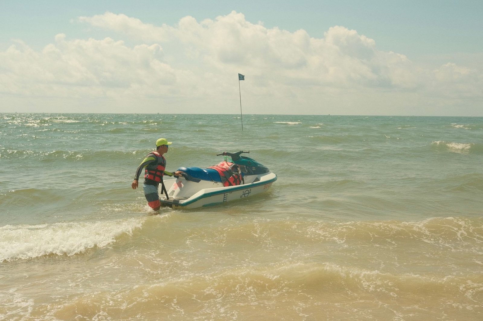 Man towing jet ski on sunny beach with waves in background.