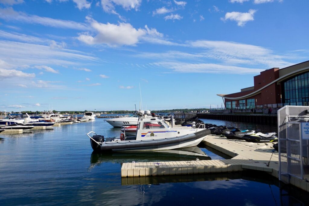 Marina with docked boats, blue sky, and waterfront buildings.