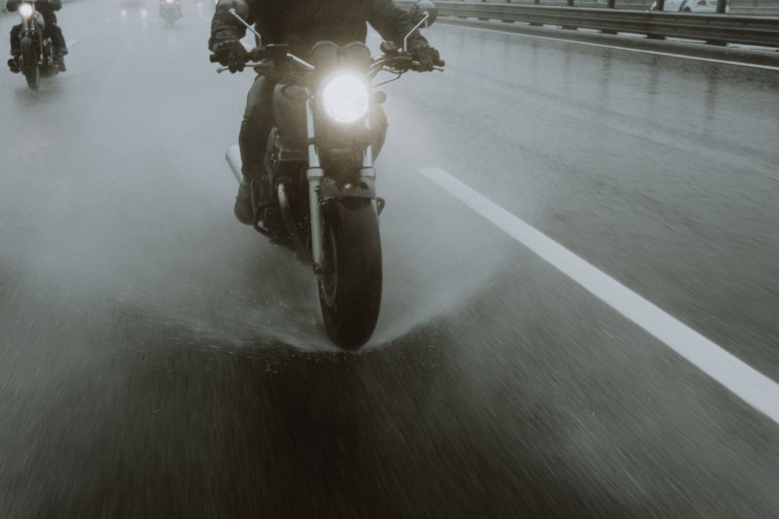 Motorcyclists riding on a wet highway at night with water splashing.