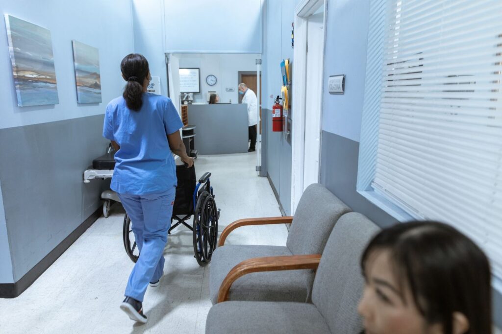 Nurse pushing wheelchair through hospital corridor.