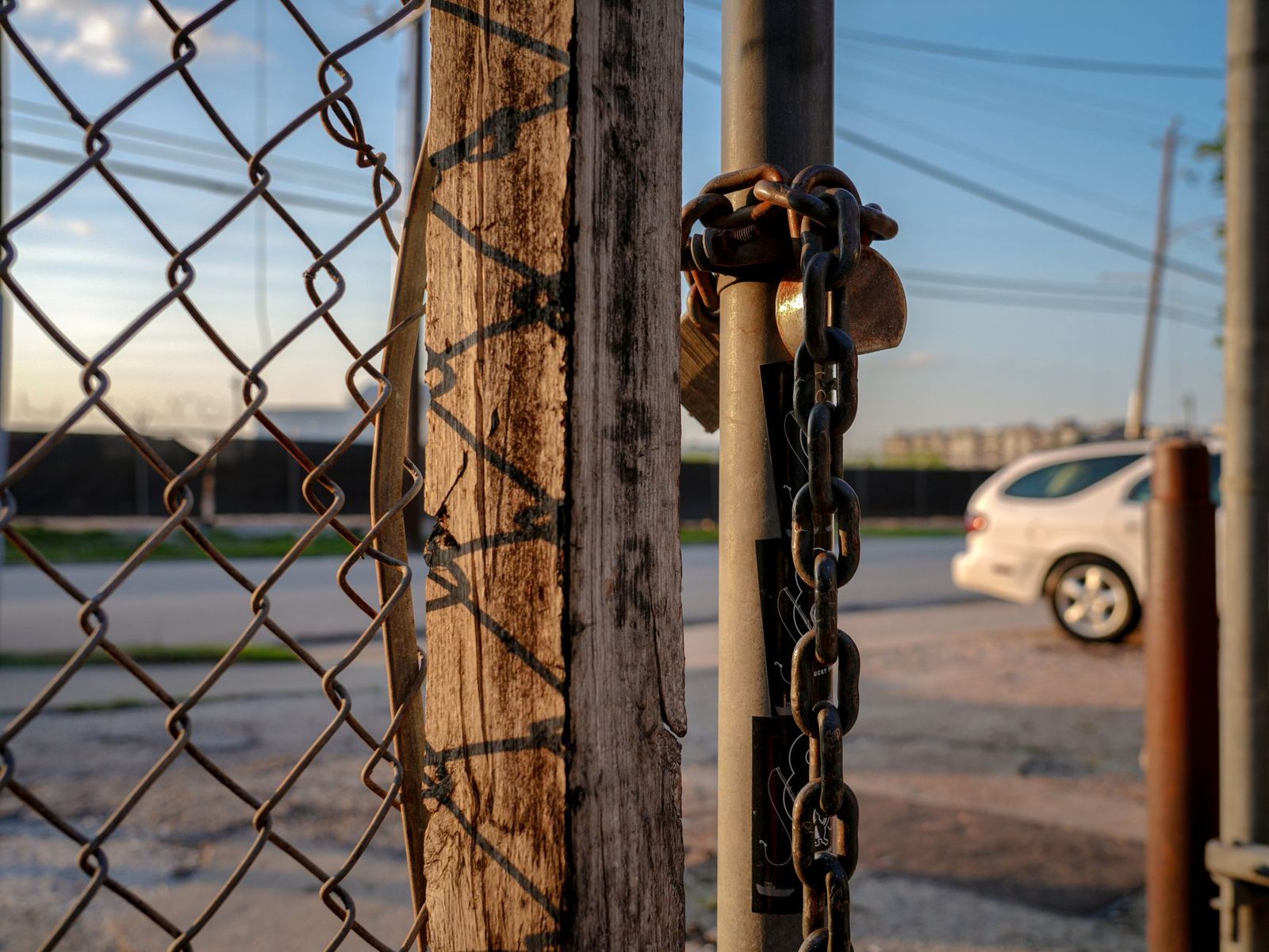 Padlock and chain on fence with car in background, representing security negligence.
