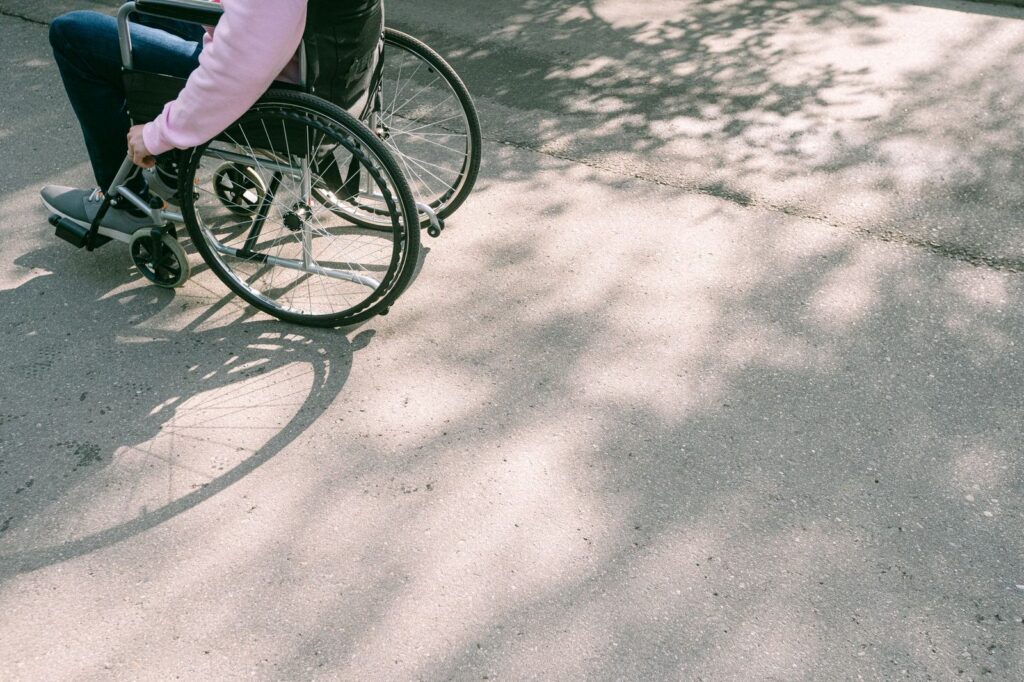 Person in wheelchair on sunlit road with tree shadows.