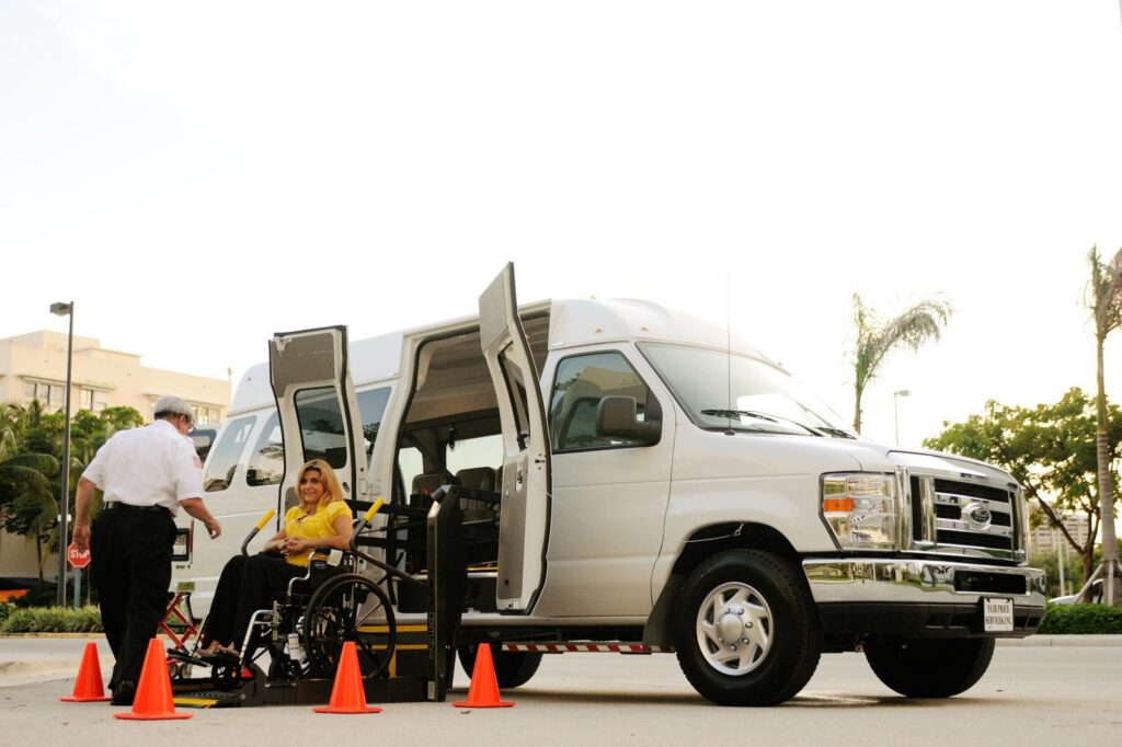 Person in wheelchair using a van lift with driver assistance outdoors.