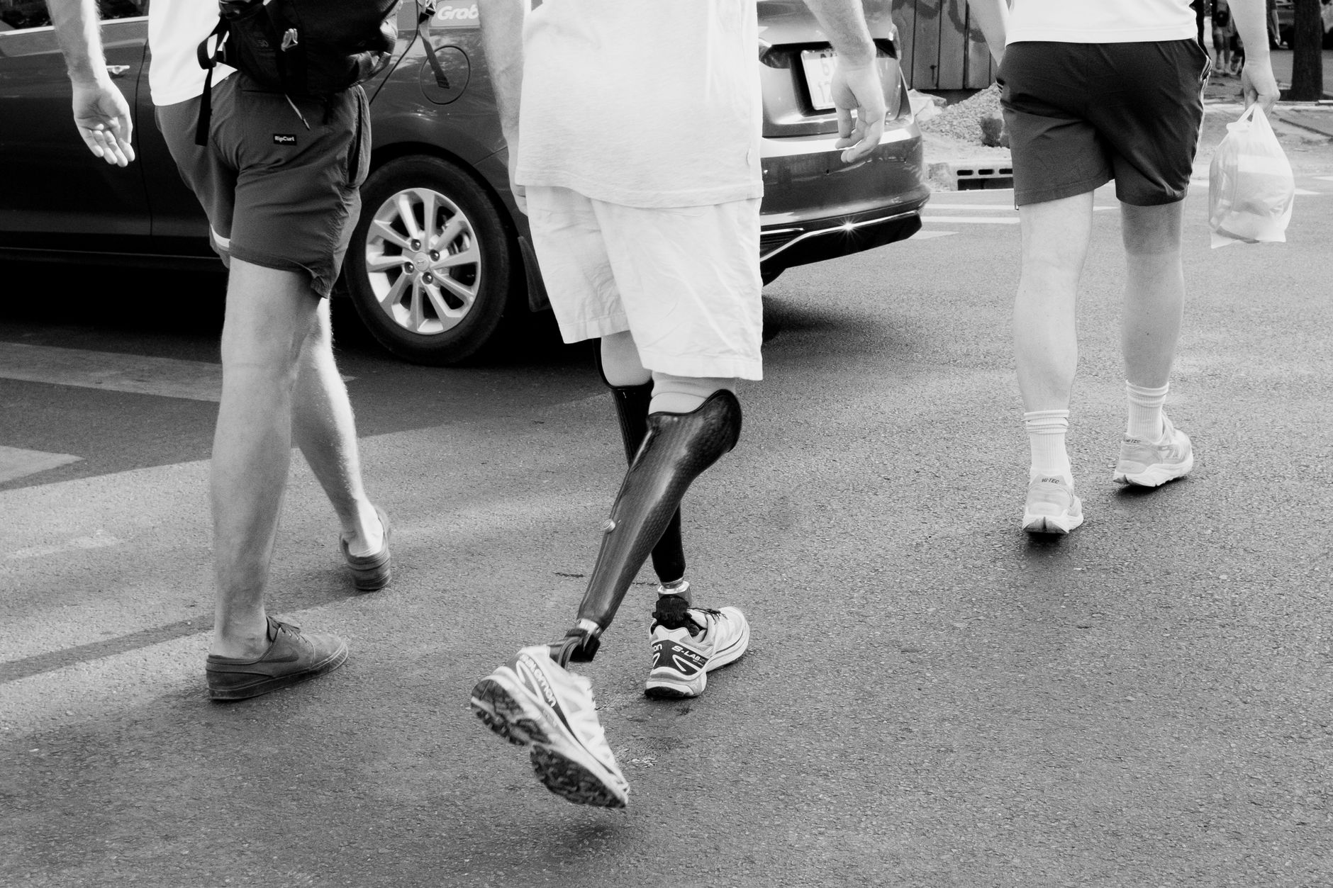 Person with a prosthetic leg walking on a city street in black and white.