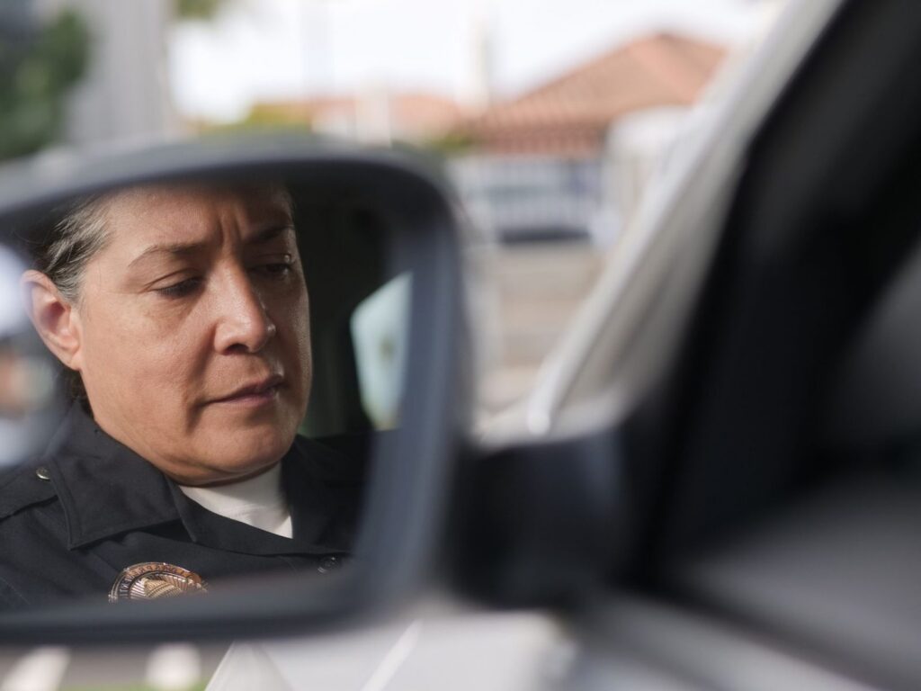 Police officer reflected in car mirror during traffic stop.