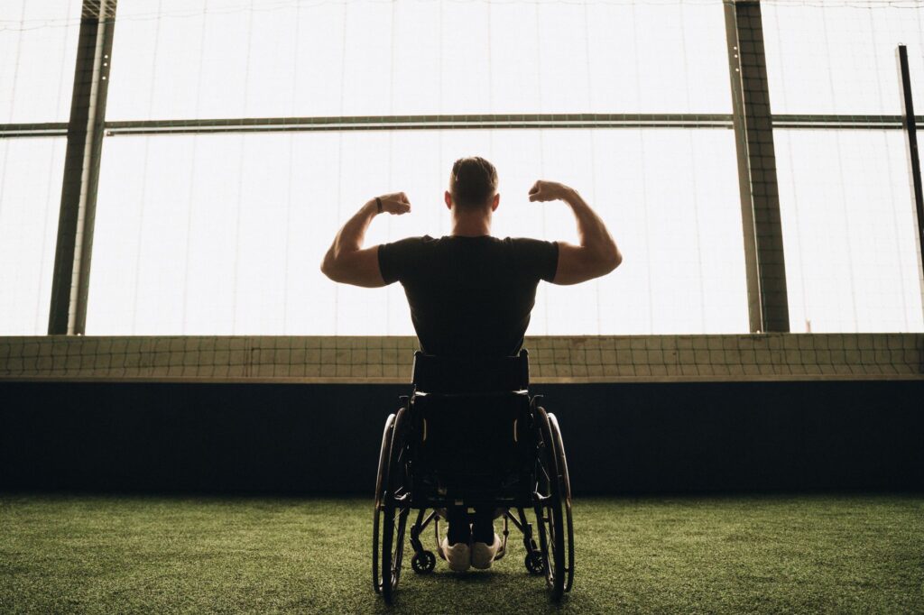 Rear view of a muscular man in a wheelchair flexing his arms in a sports facility.
