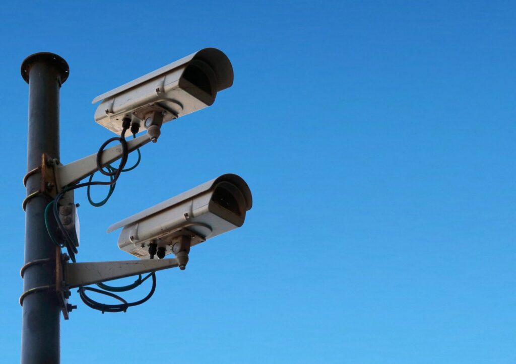 Security camera mounted on black post against blue sky outdoors.