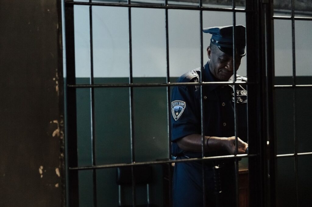 Security officer standing behind bars in dim lighting.