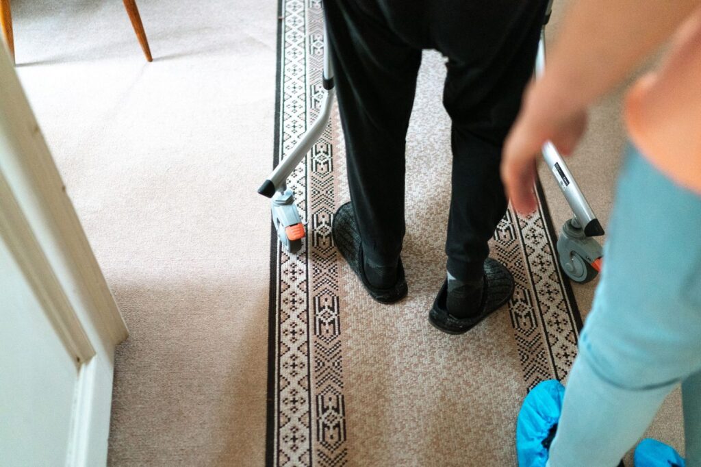 Senior person using a walker with caregiver assistance indoors.