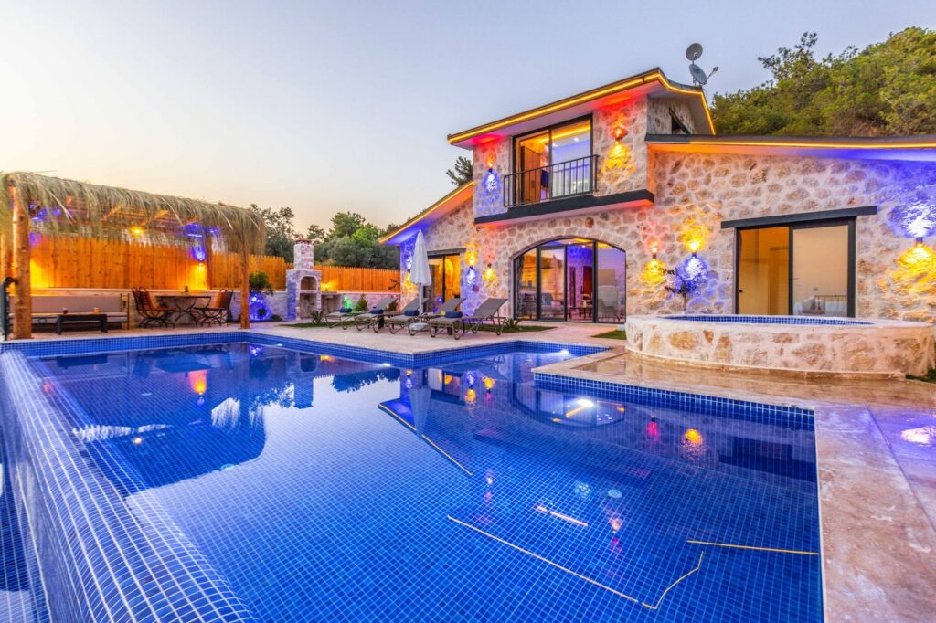 Stone villa with illuminated pool and outdoor seating area at dusk.