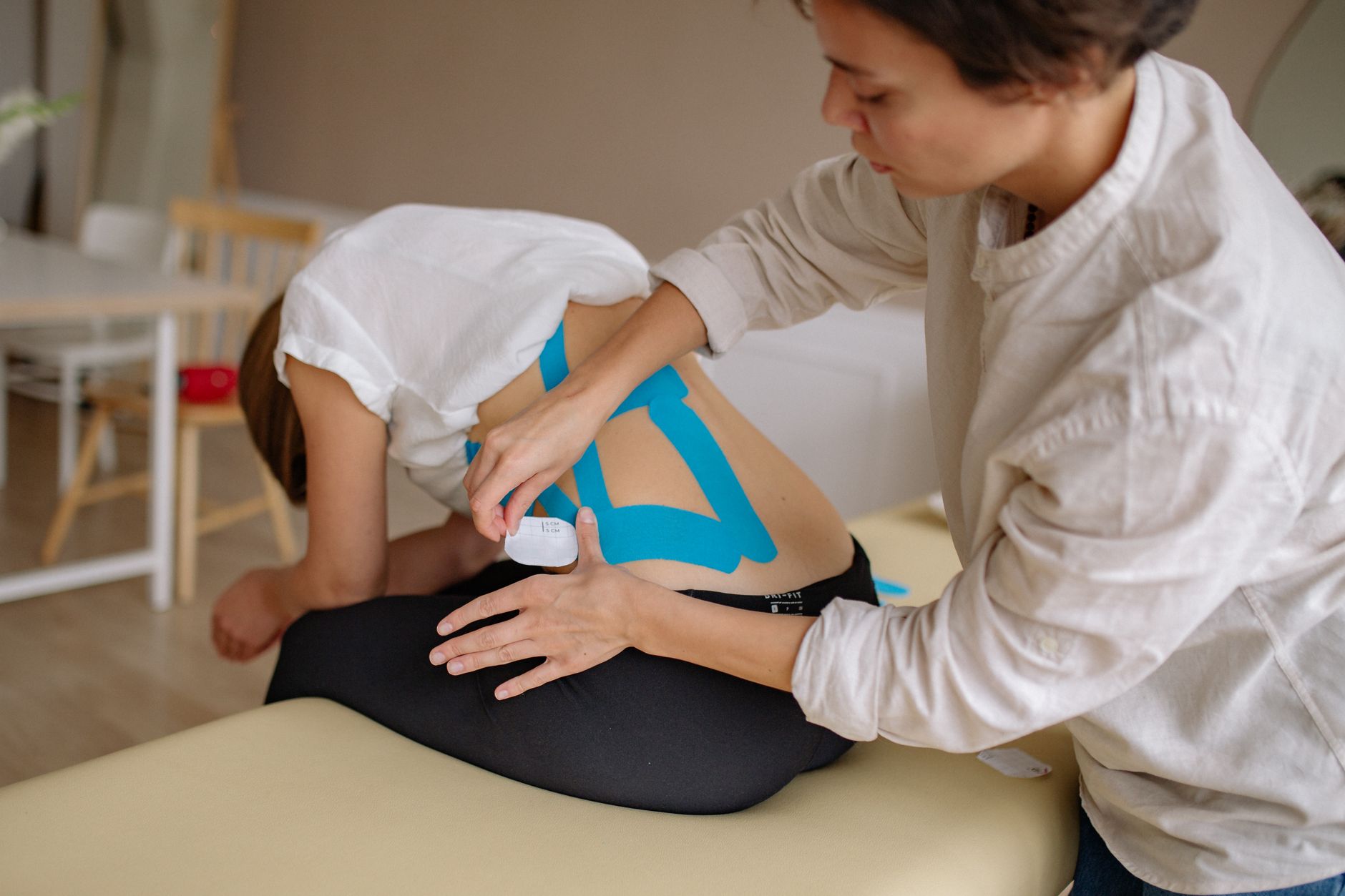 Therapist applies blue kinesiology tape to a patient's lower back in a clinic.