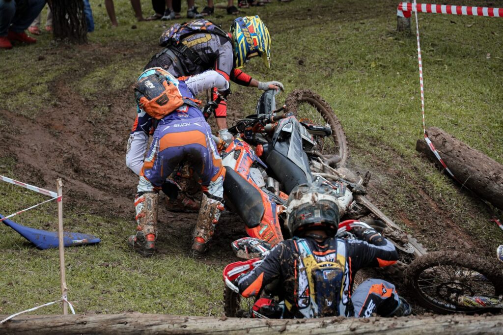 Three motorcycle riders crashed on a muddy dirt track.