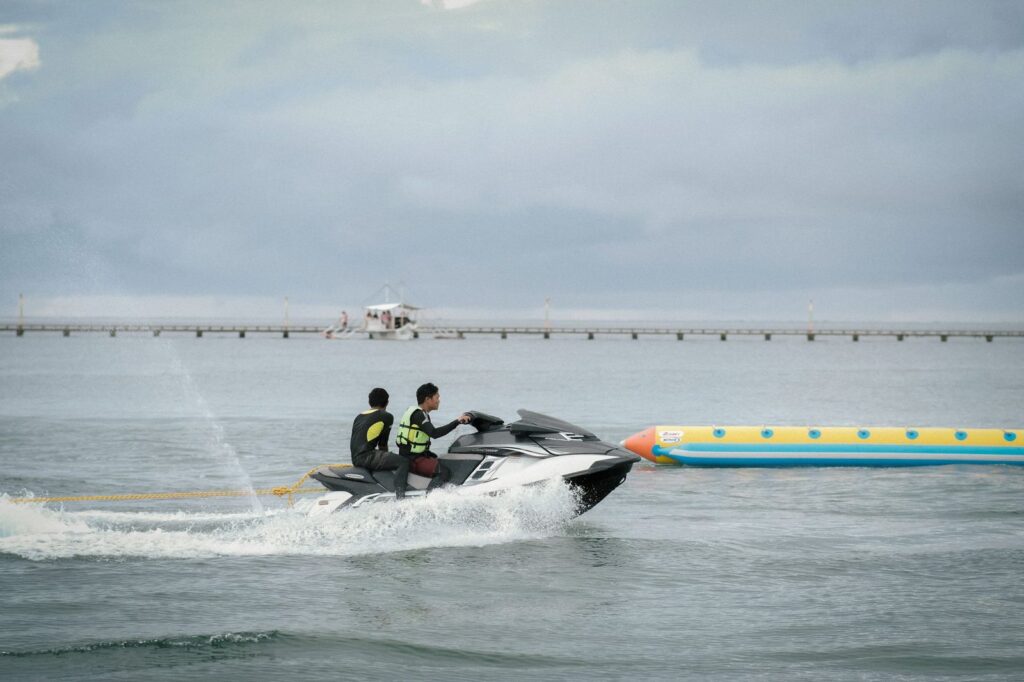 Two people ride a jet ski towing an inflatable banana boat under cloudy skies.