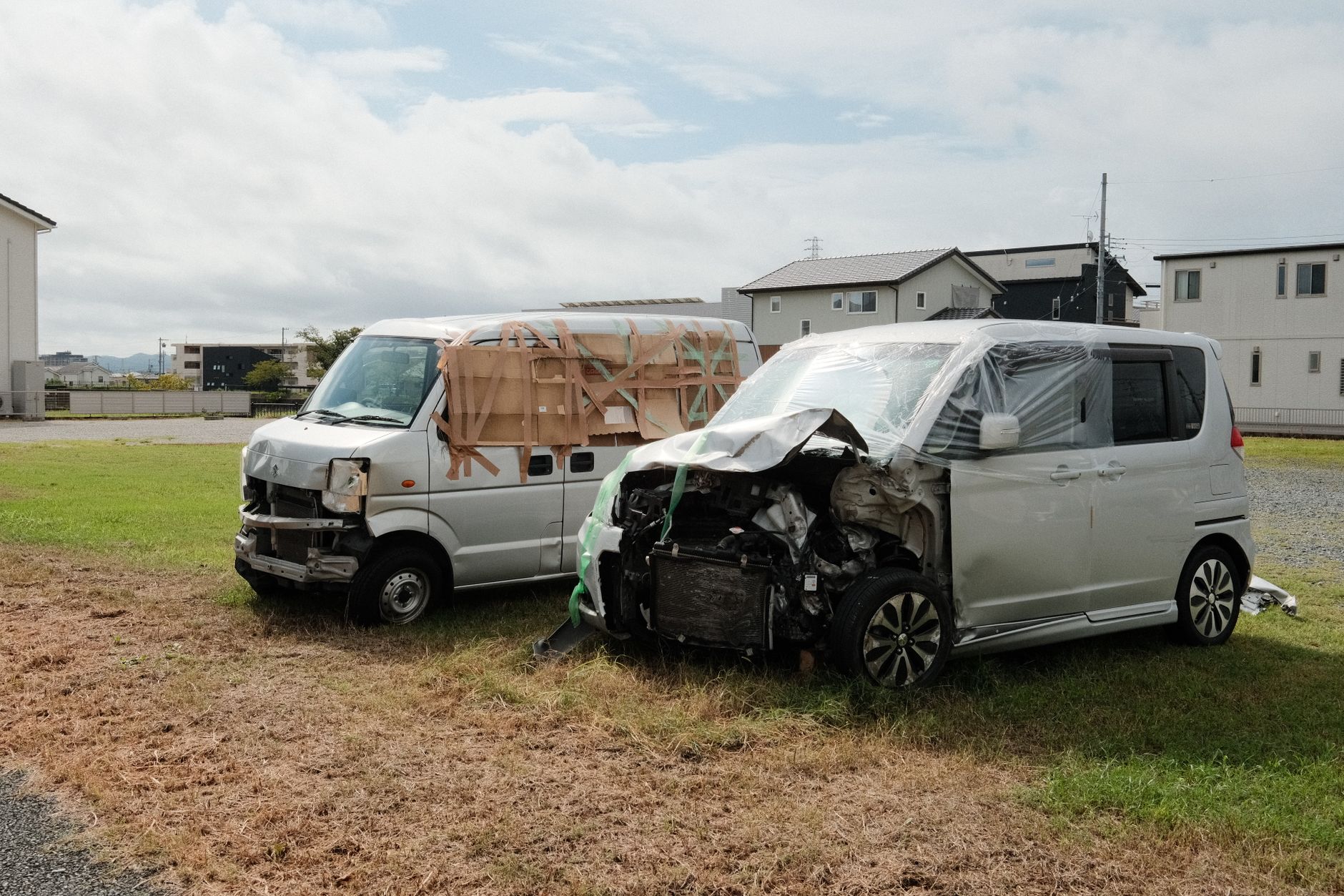 Two wrecked vans parked on a grassy area in Toyokawa, Japan.