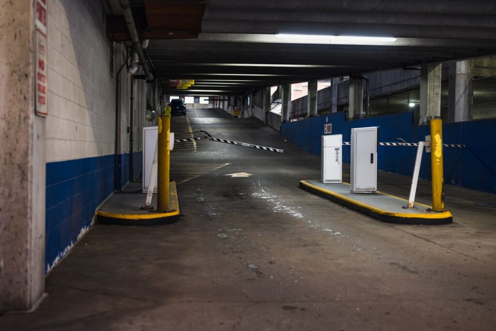 Underground parking garage entrance ramp with barriers and dim lighting.