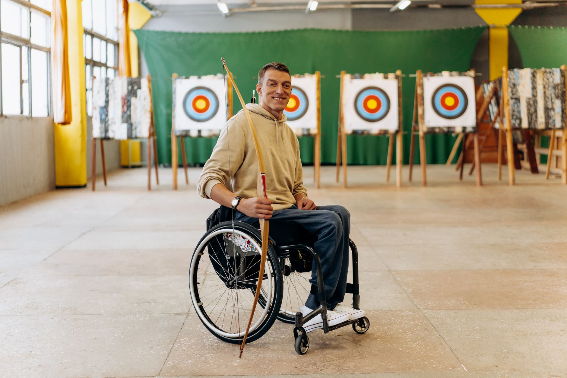 Wheelchair archer aims a bow at indoor targets during archery practice.